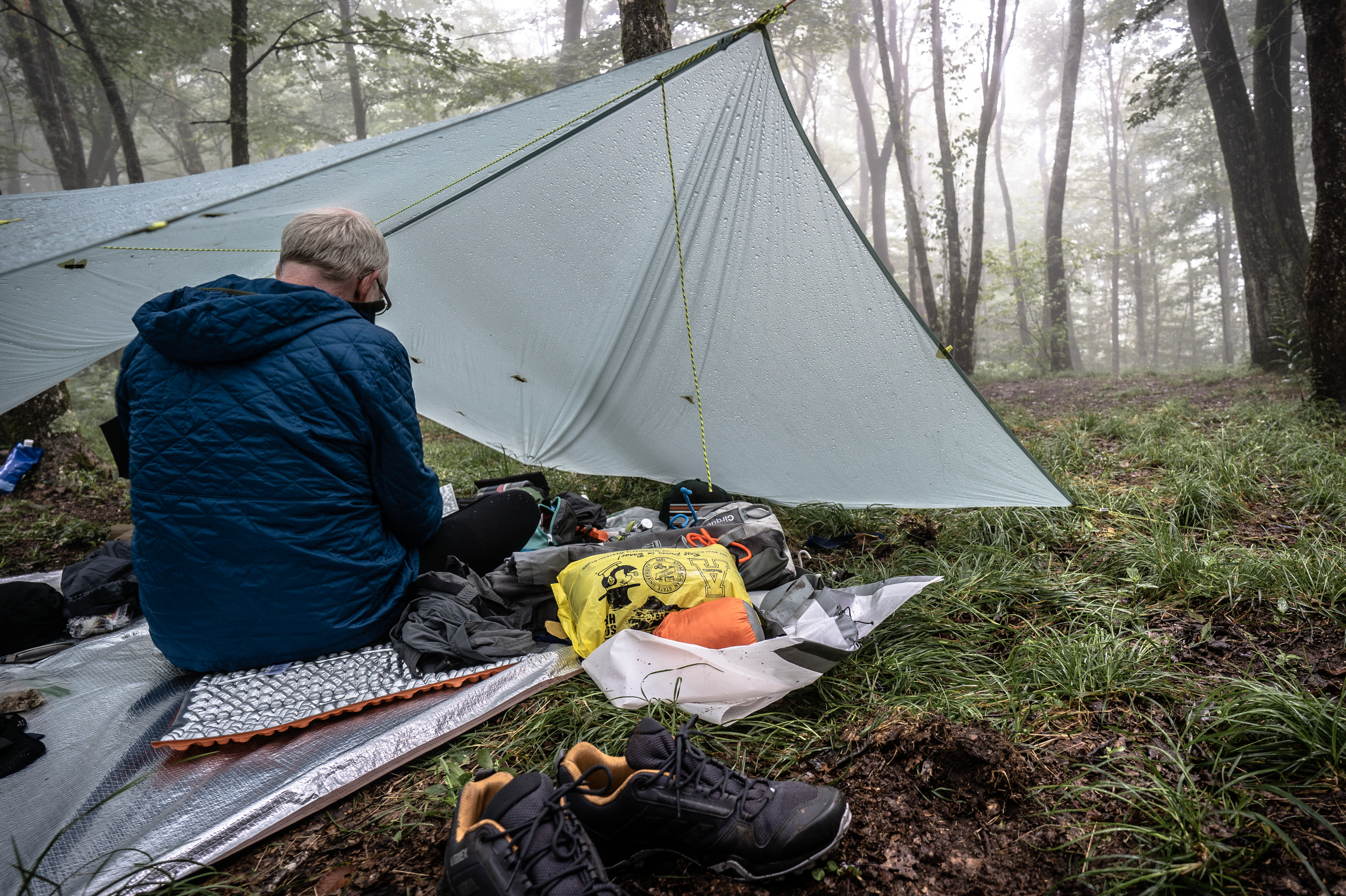 Backpacker huddled under his tarp shelter with all his gear available on the ground around him