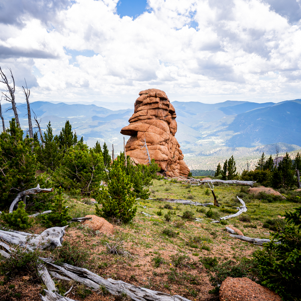A tall round rock formation sits in the middle center with the Rocky mountains in the background