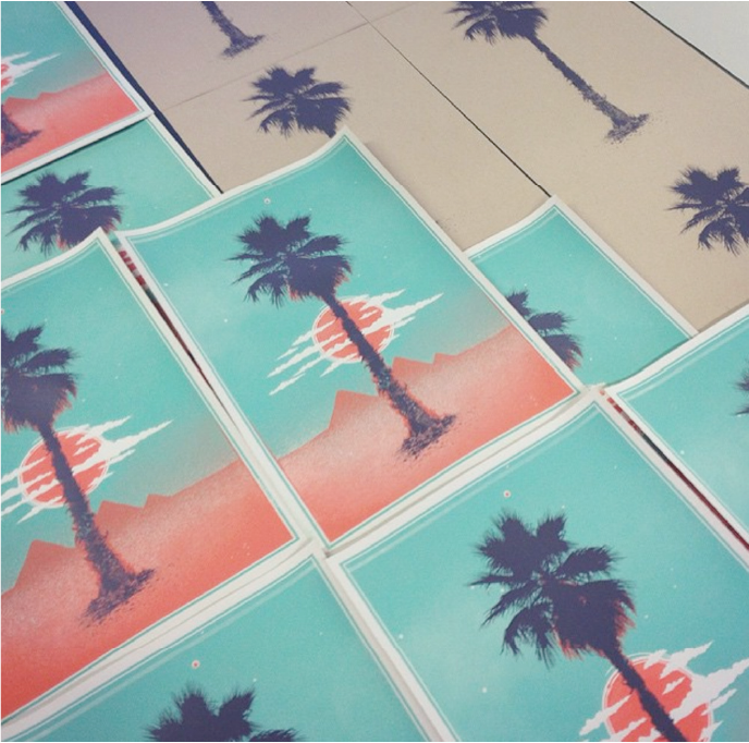 Colorful screen print of a palm tree with clouds and the sun behind