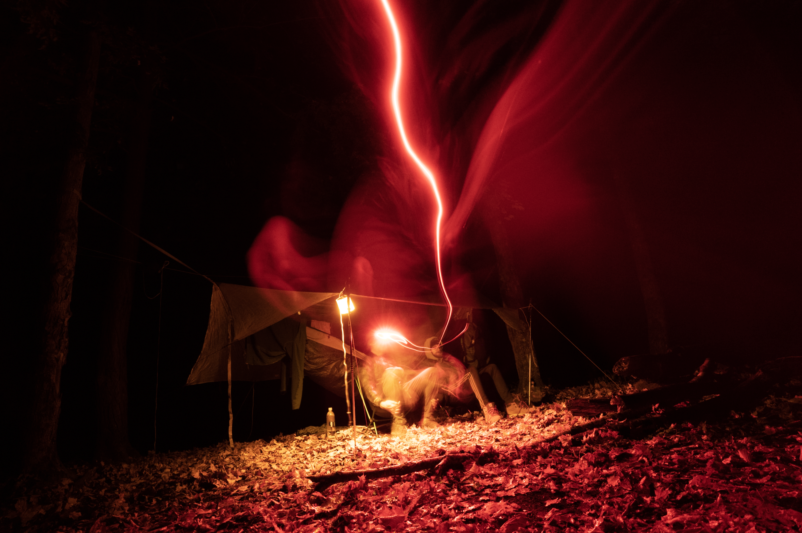 2 campers hunkered down under a tarp in the rainy dark with their headlamps radiating an eery red light